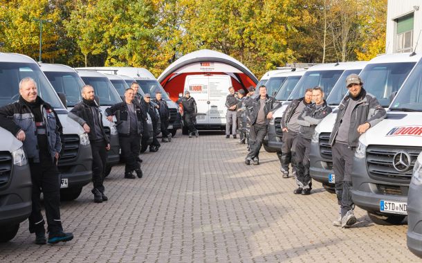 Mitarbeiter stehen auf einem großen Parkplatz vor ihren Firmenfahrzeugen